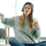 Chica sentada en el suelo escuchando música con auriculares.